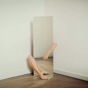 Surreal photo featuring a mirror reflecting an arm and leg on a wooden floor.