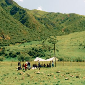 A group of people camping under a tent in a lush green mountain valley.
