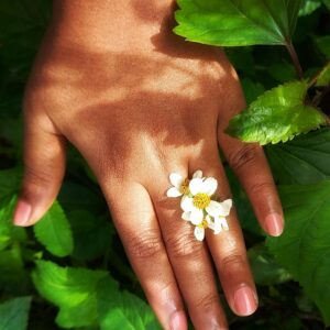 Close-up of hand with a flower ring amidst green leaves, showcasing nature's beauty.
